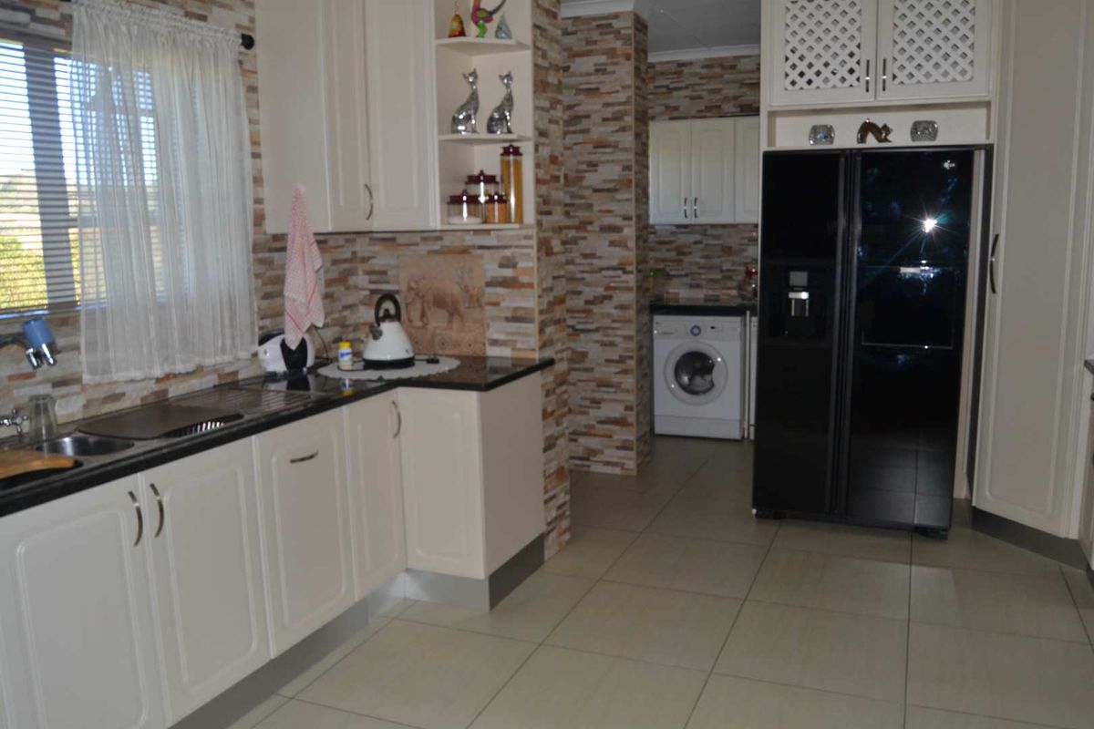 A functional kitchen featuring white cabinetry, dark countertops, stone-cladding wall accents, and integrated laundry space with tiled flooring.