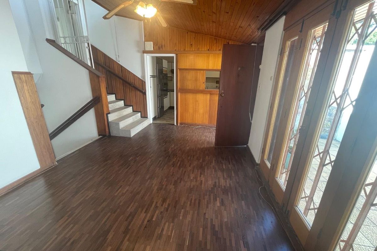 Spacious living area featuring wooden parquet flooring, a vaulted timber ceiling, and direct access to the patio through security-fitted glass doors.