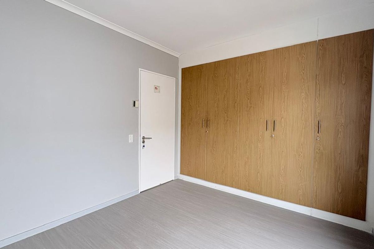 A clean, empty bedroom featuring light grey laminate flooring, neutral walls, and extensive built-in wooden cupboards providing ample storage space.