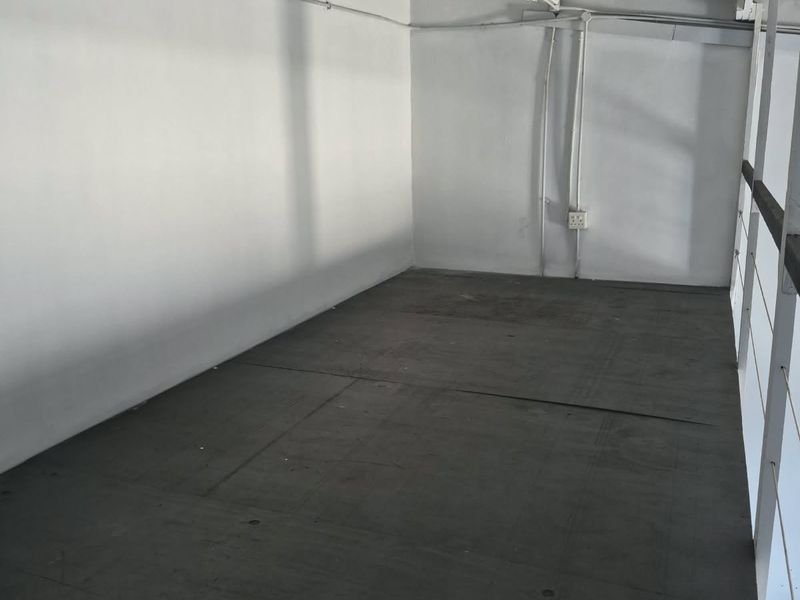 An empty industrial utility space featuring exposed ceiling beams, surface-mounted electrical conduits, and a metal safety railing.