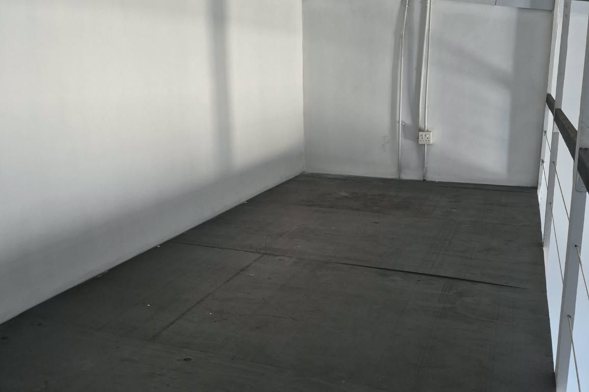 An empty industrial utility space featuring exposed ceiling beams, surface-mounted electrical conduits, and a metal safety railing.