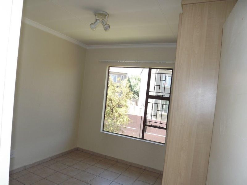 A bright, empty bedroom featuring tiled flooring, a built-in wardrobe, and a window fitted with security bars.