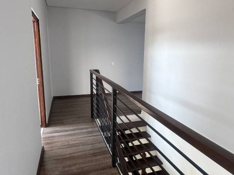 A bright, modern hallway featuring timber-look laminate flooring and a contemporary staircase with a dark timber handrail and metal balustrade.