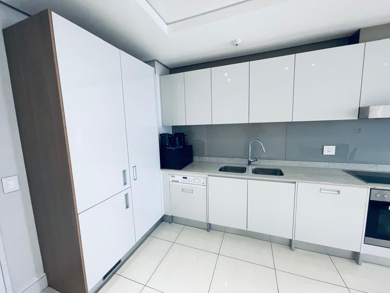 Modern kitchen featuring white high-gloss cabinetry, stone countertops, integrated appliances, and a sleek glass splashback in a clean, minimalist design.