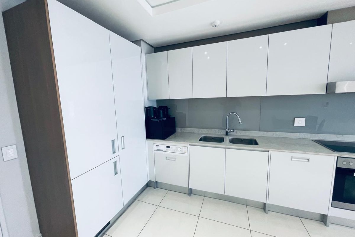 Modern kitchen featuring white high-gloss cabinetry, stone countertops, integrated appliances, and a sleek glass splashback in a clean, minimalist design.