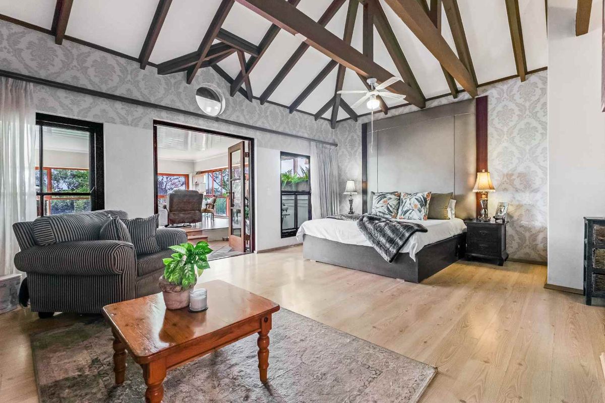 Spacious bedroom featuring exposed timber ceiling beams, laminate flooring, and direct access to an adjoining patio through double doors.
