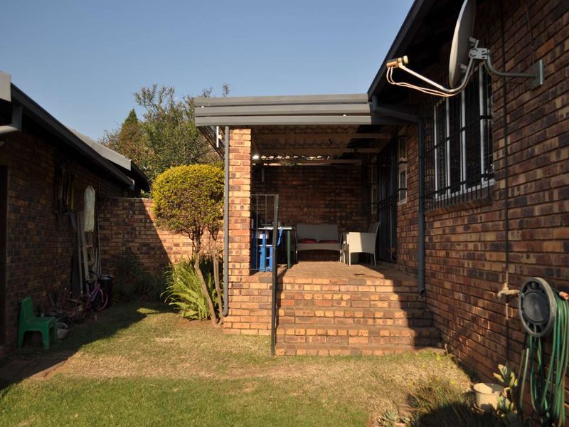 A rear view of the townhouse featuring a brick facade, a covered patio area with steps, and a small garden space.