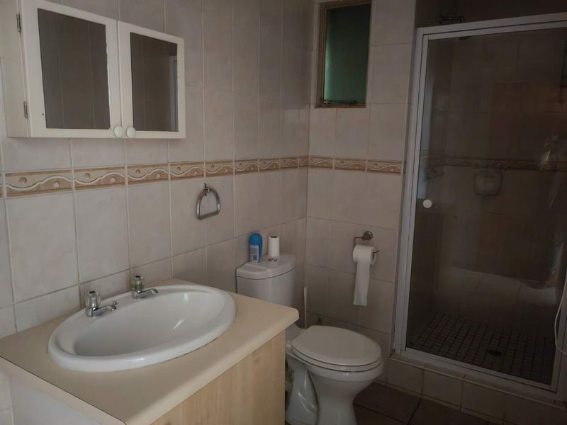 A dated bathroom featuring a vanity cabinet, ceramic basin, toilet, and a separate shower enclosure with tiled walls.