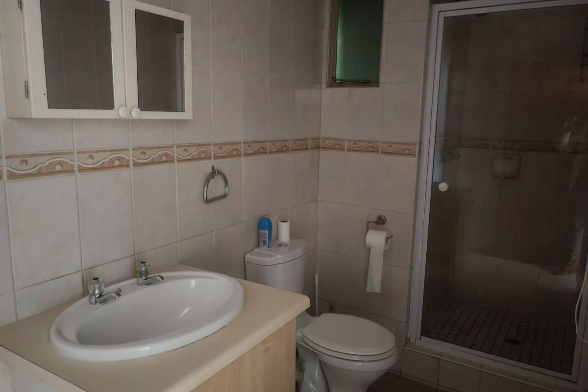 A dated bathroom featuring a vanity cabinet, ceramic basin, toilet, and a separate shower enclosure with tiled walls.