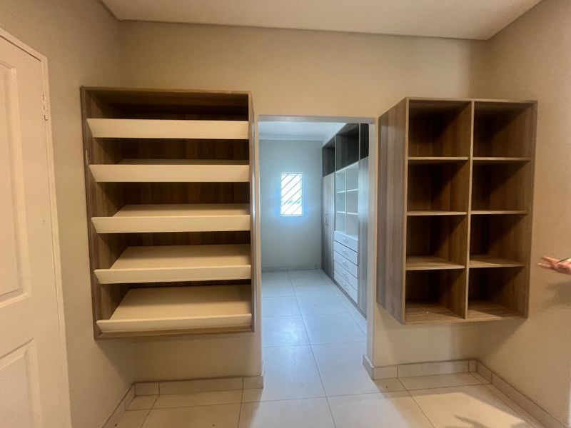 A walk-in closet or dressing area featuring extensive built-in shelving and cabinetry with neutral tiled flooring and a small window.