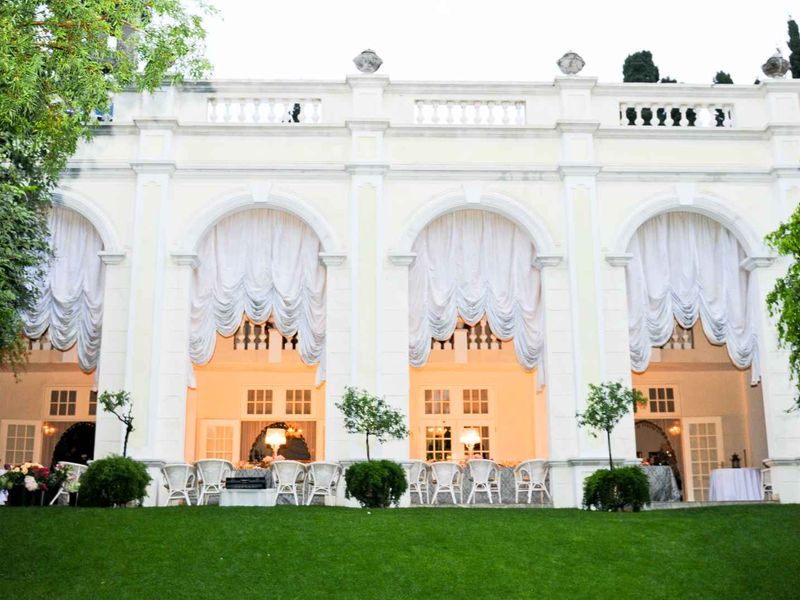 Elegant rear facade of a guest house featuring a grand arched colonnade, classic balustrade detailing, and multiple sets of French doors opening to the garden.