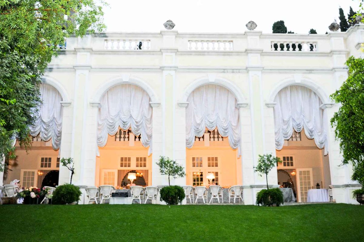 Elegant rear facade of a guest house featuring a grand arched colonnade, classic balustrade detailing, and multiple sets of French doors opening to the garden.
