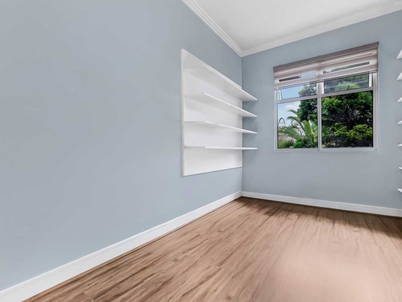 A bright, empty bedroom featuring light blue walls, modern laminate flooring, and built-in white shelving units.