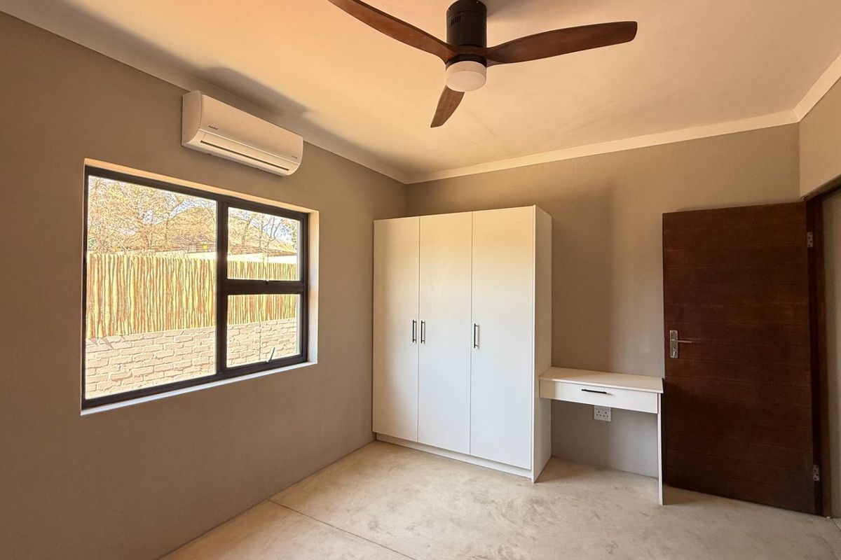 A well-maintained bedroom featuring neutral walls, a built-in wardrobe, a ceiling fan, and a wall-mounted air conditioning unit.
