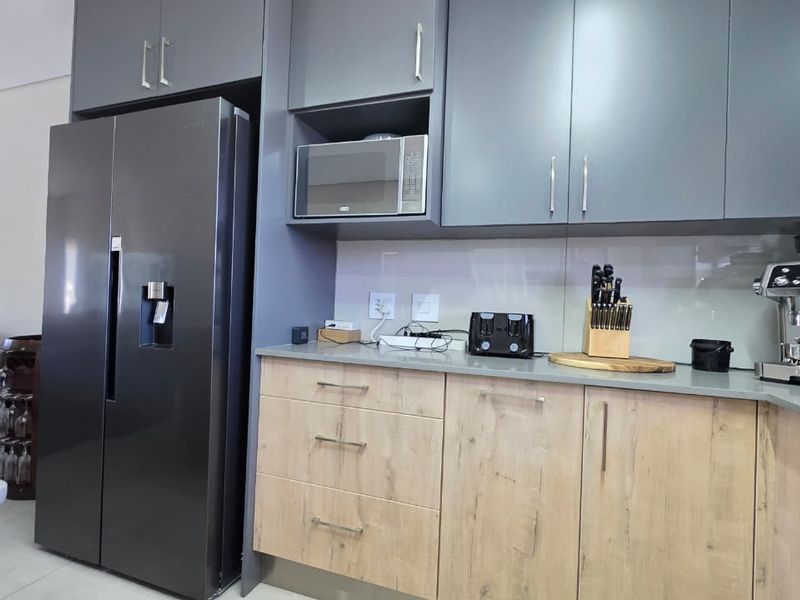 Modern kitchen featuring sleek grey upper cabinetry, light wood-finish lower cabinets, stone countertops, and a built-in microwave.