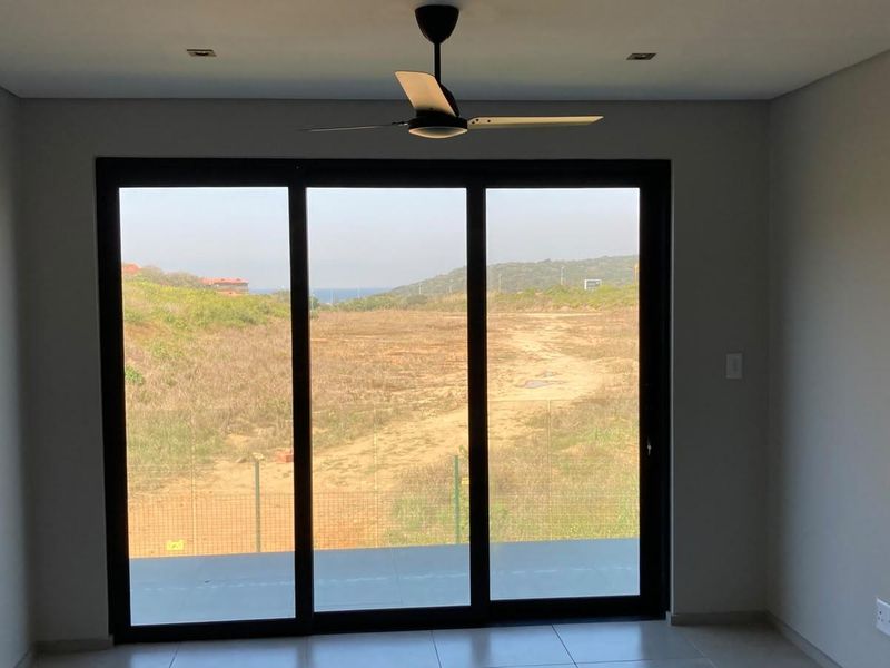 An empty living room featuring modern tiled flooring, a ceiling fan, and large sliding glass doors that provide natural light and scenic outdoor views.