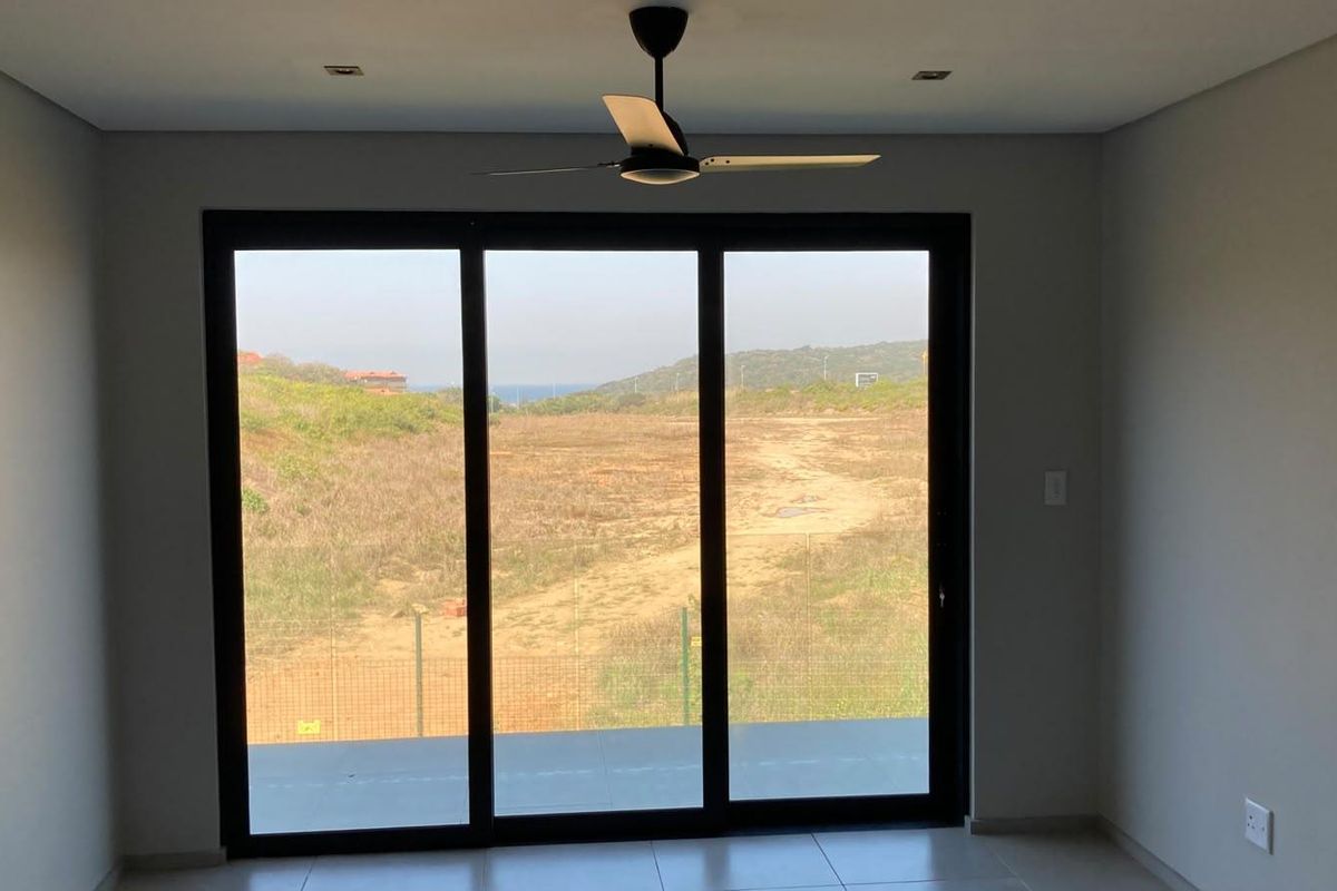 An empty living room featuring modern tiled flooring, a ceiling fan, and large sliding glass doors that provide natural light and scenic outdoor views.