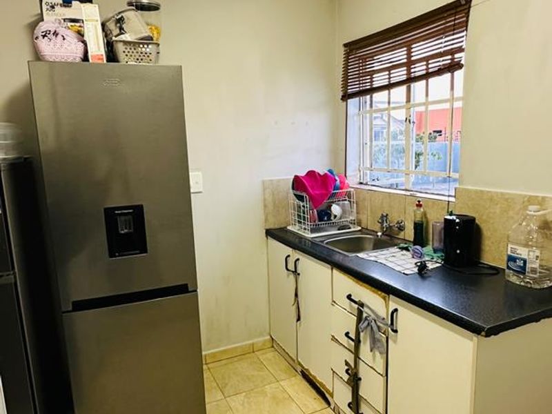 A functional scullery area featuring tiled flooring, built-in cabinetry with a sink, and a window providing natural light.