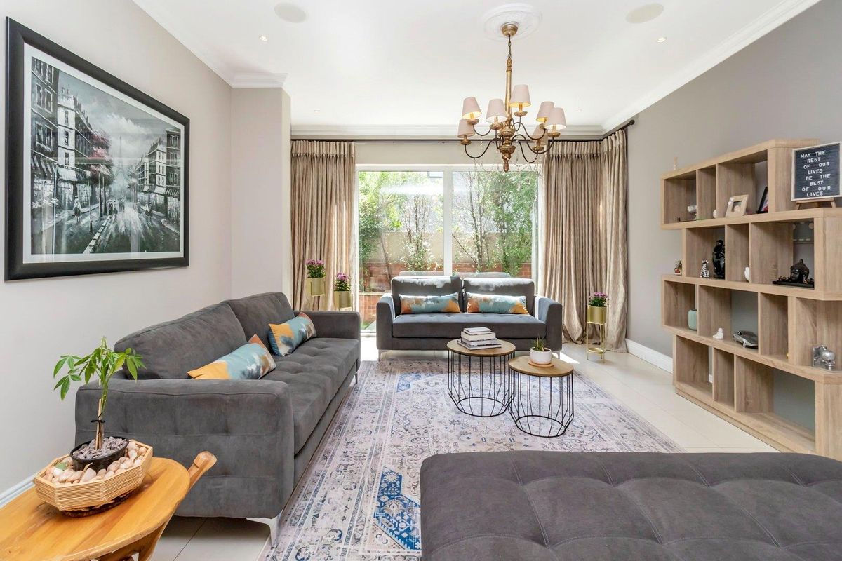 A well-maintained living room featuring recessed ceiling lighting, a decorative chandelier, and large sliding glass doors providing access to the rear garden.