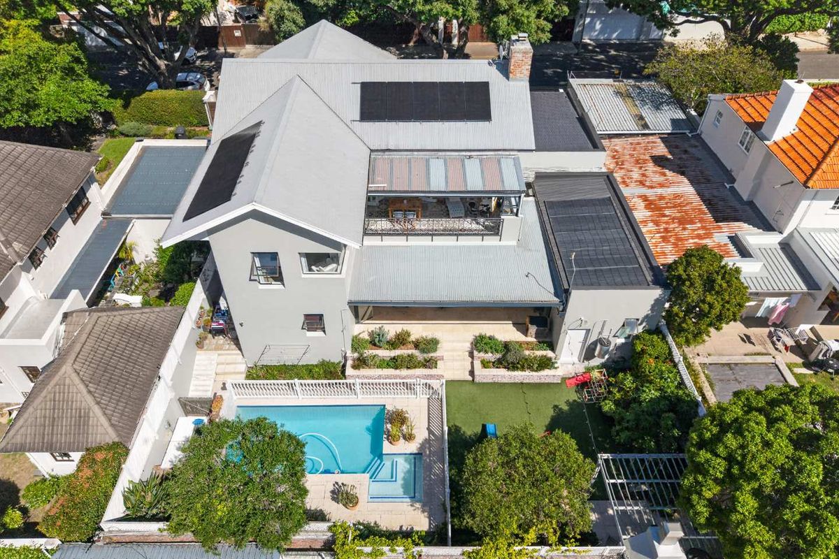 Aerial view of a residential property featuring a swimming pool, landscaped garden, patio area, and a multi-level house with solar panels on the roof.