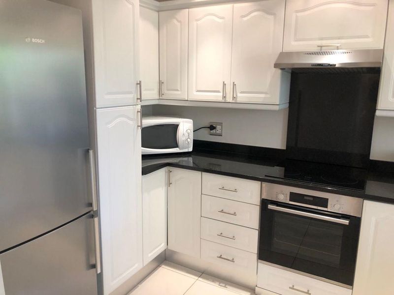 A well-maintained kitchen featuring white cabinetry, black granite countertops, and integrated stainless steel appliances including an oven, hob, and refrigerator.