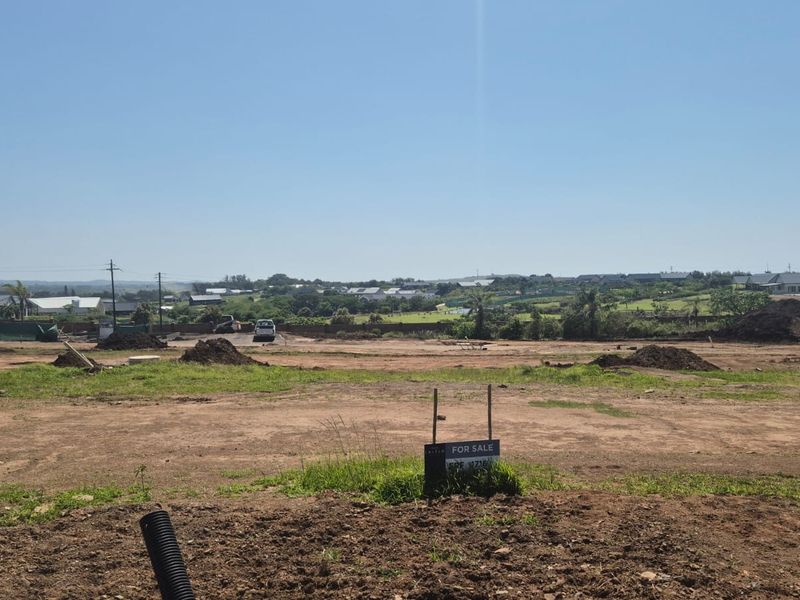 A wide-angle view of a vacant residential plot of land with a for sale sign, situated in a developing neighborhood.