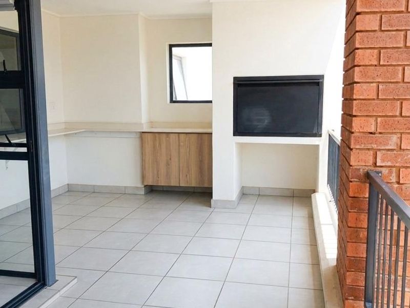 A spacious covered balcony featuring tiled flooring, a built-in braai, and convenient built-in cabinetry with a countertop, perfect for outdoor entertaining.