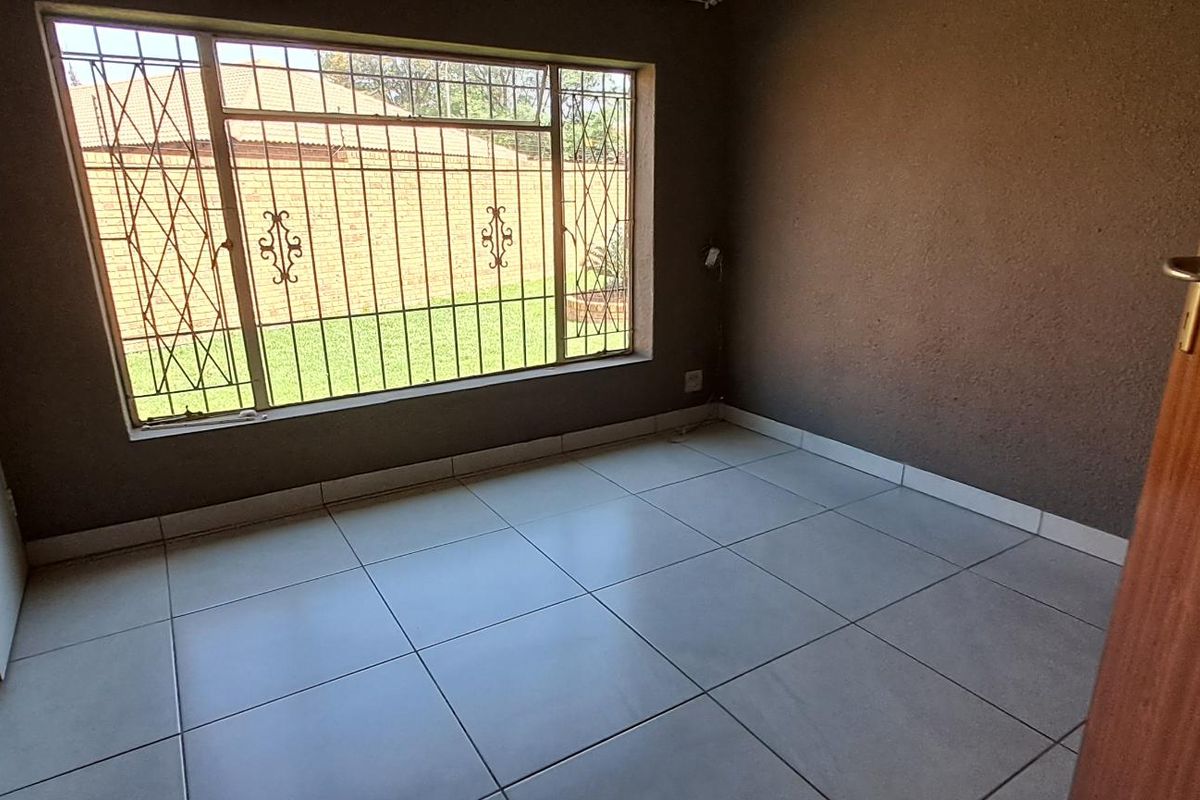 A vacant bedroom featuring large windows with security bars, tiled flooring, and built-in cupboards.