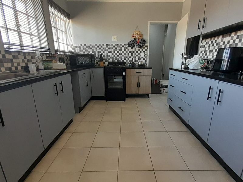 A functional kitchen featuring grey cabinetry, a black countertop, a checkered tile backsplash, and ceramic floor tiles with ample storage space.