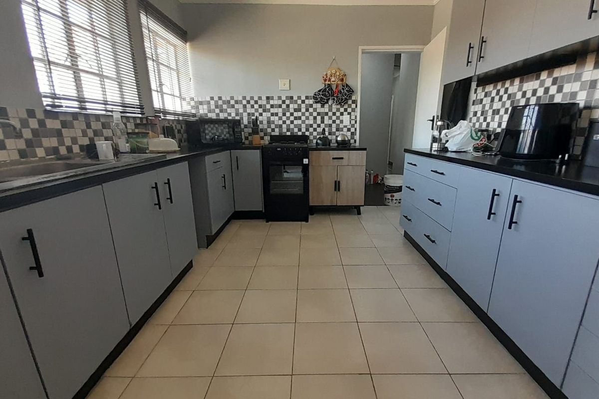 A functional kitchen featuring grey cabinetry, a black countertop, a checkered tile backsplash, and ceramic floor tiles with ample storage space.
