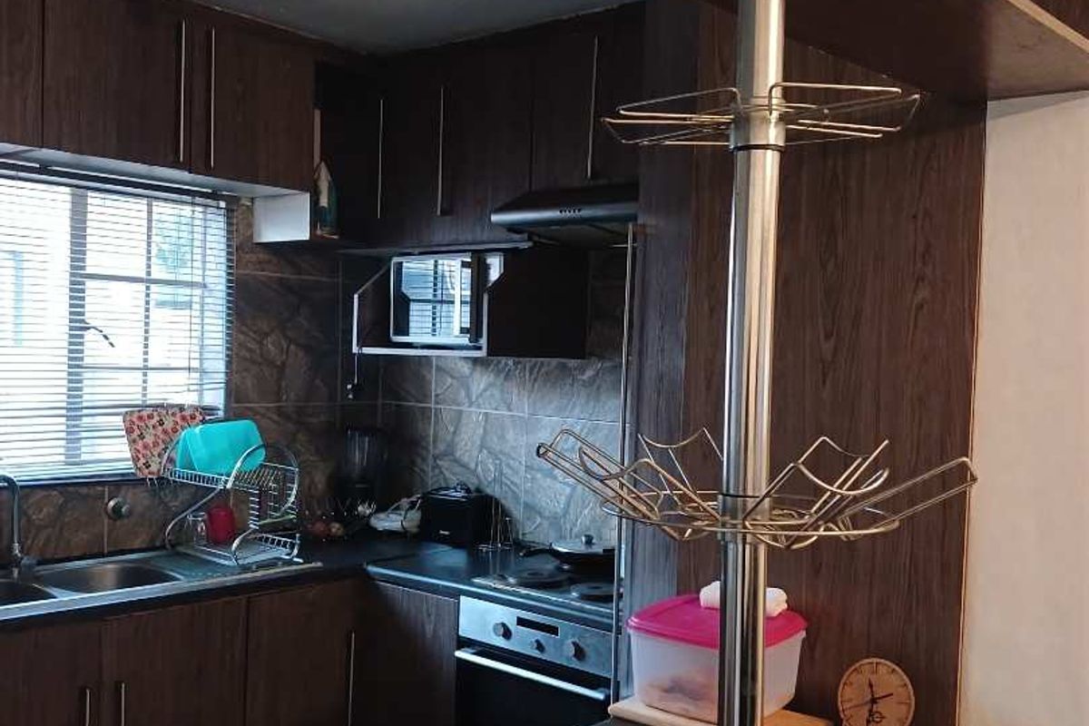 A functional kitchen featuring dark wood-look cabinetry, a built-in oven with extractor fan, stainless steel sink, and tiled splashbacks.