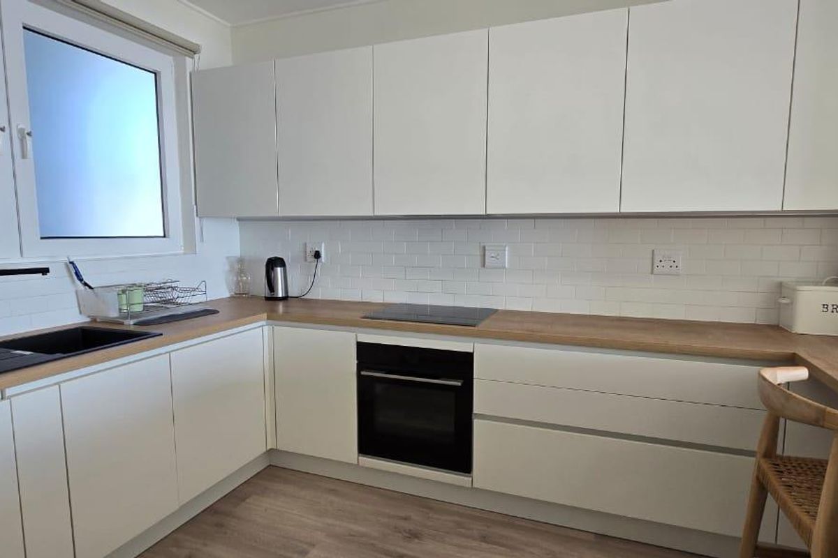 Modern kitchen featuring white cabinetry, wood-look countertops, subway tile backsplash, and integrated appliances including an oven and hob.