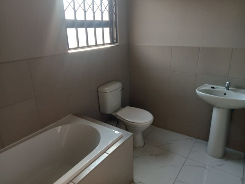 A functional bathroom featuring a bathtub, pedestal sink, and toilet with neutral wall and floor tiling.