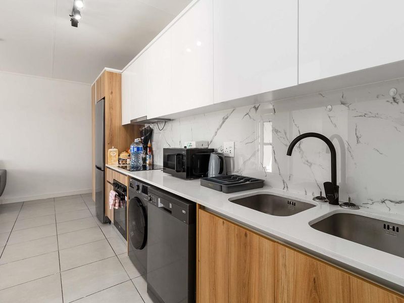 Modern galley-style kitchen featuring white high-gloss cabinetry, wood-grain lower cupboards, marble-look splashback, and integrated appliances with a sleek black tap.