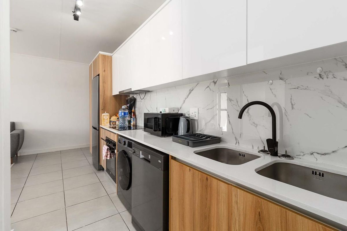 Modern galley-style kitchen featuring white high-gloss cabinetry, wood-grain lower cupboards, marble-look splashback, and integrated appliances with a sleek black tap.