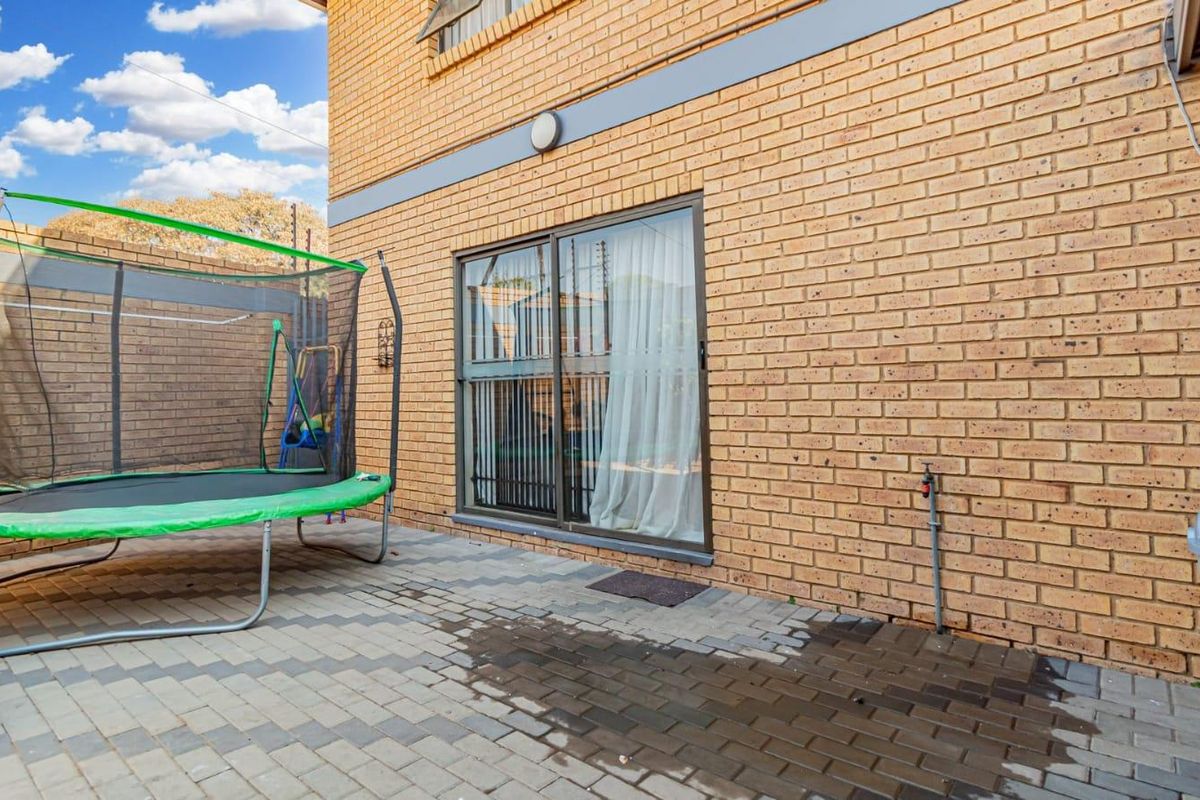 A rear exterior view of the townhouse featuring a brick facade, a paved patio area, and a sliding glass door providing access to the interior.