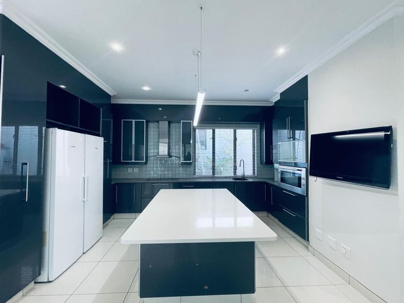 Modern kitchen featuring high-gloss cabinetry, a central island with quartz countertops, built-in oven, extractor fan, and sleek tiled flooring.