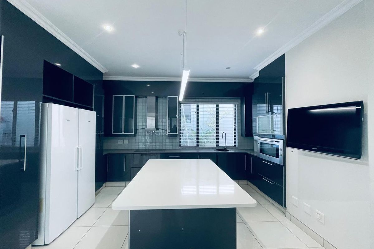 Modern kitchen featuring high-gloss cabinetry, a central island with quartz countertops, built-in oven, extractor fan, and sleek tiled flooring.