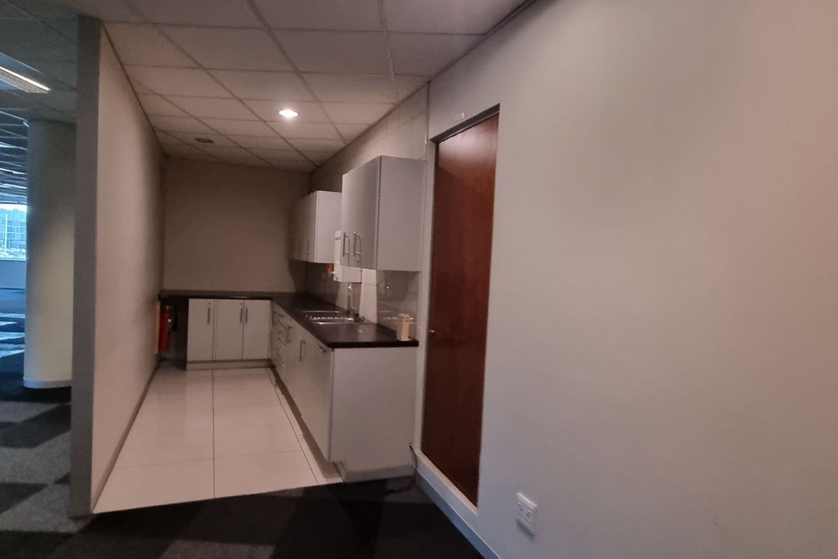 A functional office kitchenette area featuring built-in cabinetry, a sink, and tiled flooring, situated adjacent to an open-plan office workspace.