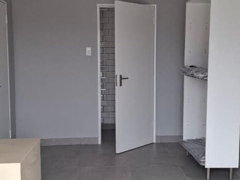 A clean, modern office space featuring neutral grey walls, large format floor tiles, and recessed ceiling lighting.