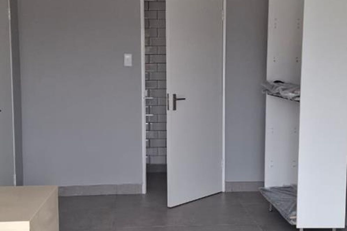 A clean, modern office space featuring neutral grey walls, large format floor tiles, and recessed ceiling lighting.