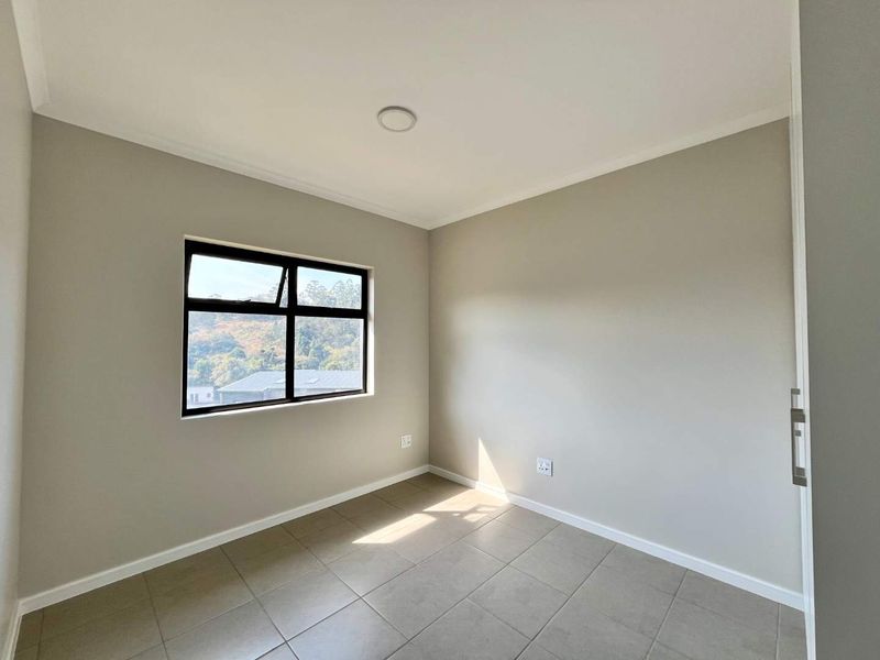 A bright, empty bedroom featuring neutral tiled flooring, a built-in cupboard, and an aluminium-framed window with natural light.