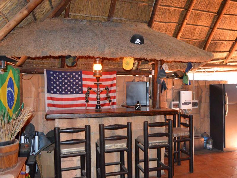 Rustic outdoor-style bar area featuring a thatched roof, stone wall cladding, and a built-in bar counter with tiled flooring.