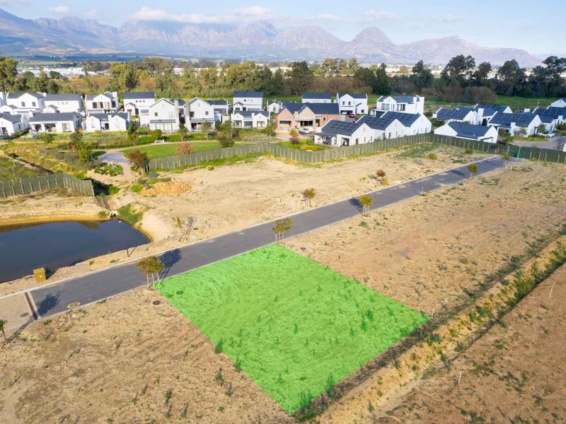 An aerial view of a vacant residential plot in a developed estate, featuring road access and scenic mountain views in the background.