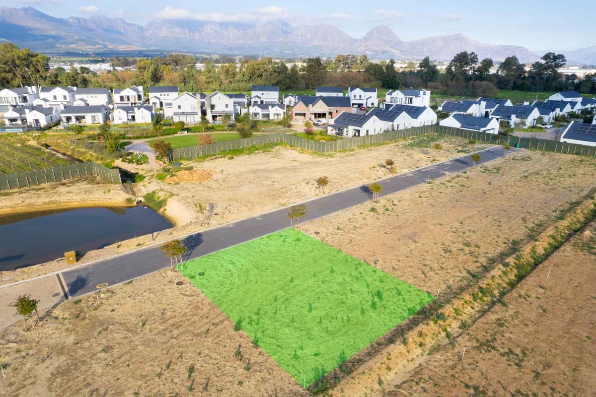 An aerial view of a vacant residential plot in a developed estate, featuring road access and scenic mountain views in the background.