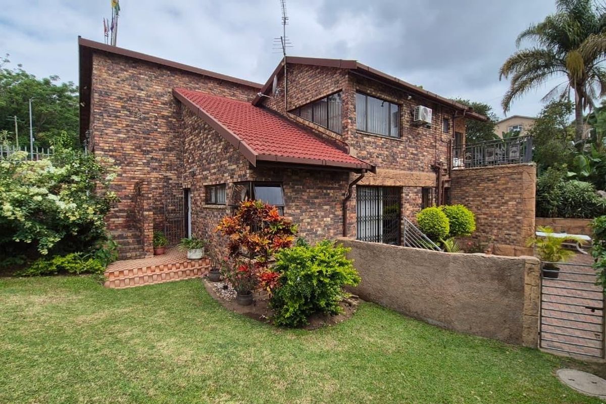 Rear view of a multi-level face-brick house featuring a tiled roof, established garden, and paved access areas.