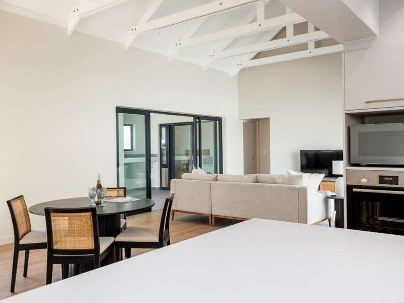 Spacious open-plan living and dining area featuring vaulted ceilings with exposed rafters, modern kitchen appliances, and seamless access to the patio through sliding doors.