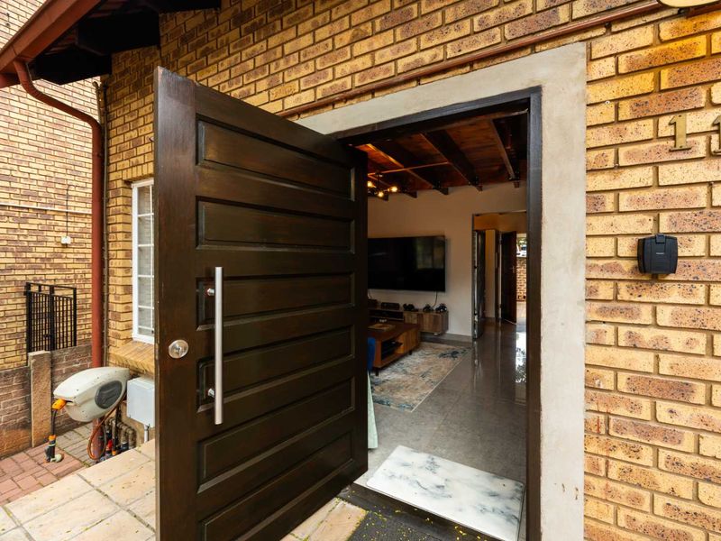 A welcoming entrance featuring a modern timber pivot door, exposed brick exterior, and a glimpse into the open-plan living area with exposed ceiling beams.
