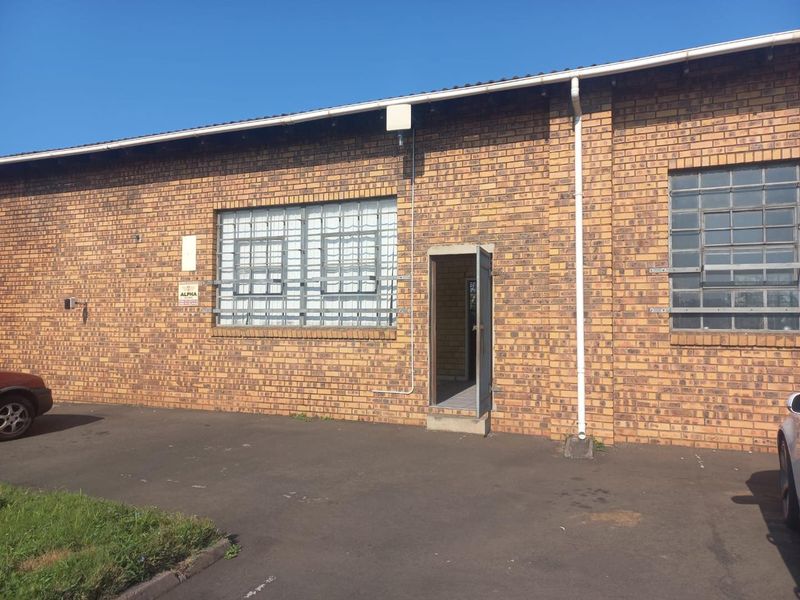 Front exterior view of an industrial building featuring face brick construction, steel-framed windows with security bars, and an asphalt driveway.