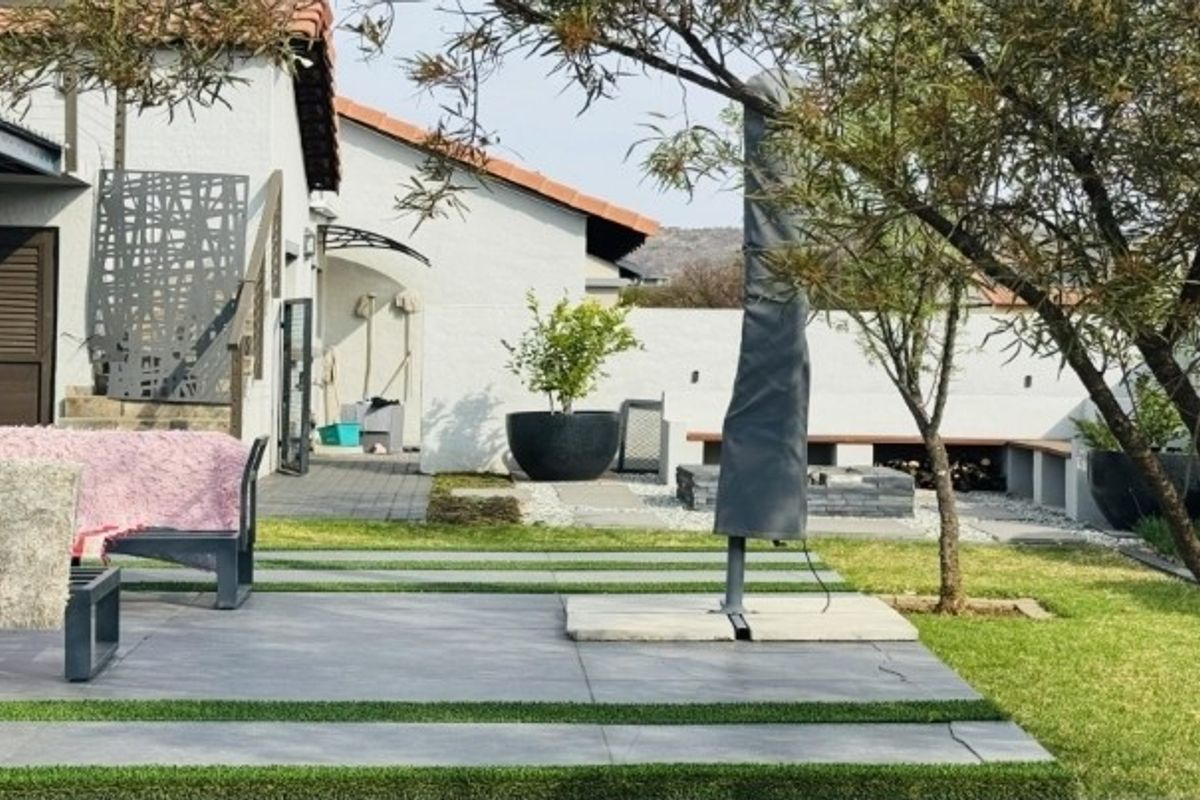 A well-maintained rear garden featuring a paved patio area, built-in bench seating, a fire pit, and decorative metal screening against the house facade.